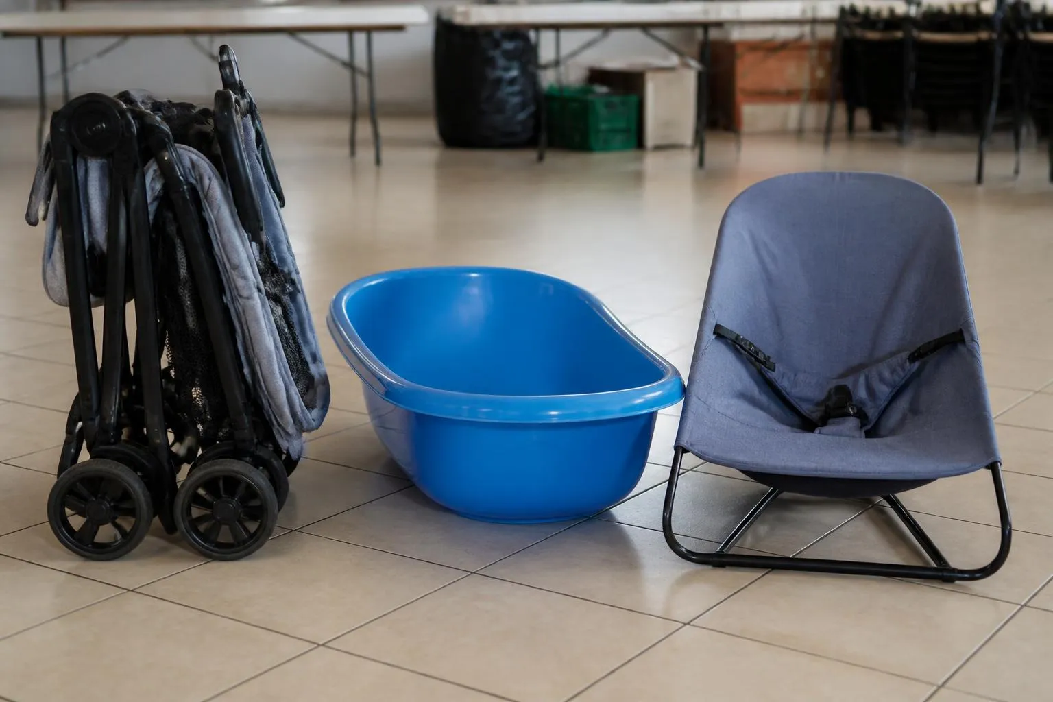 Poussette pliée, baignoire en plastique et transat posés côte à côte sur le carrelage d'une salle de dépôt